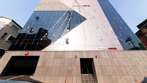 A modern hotel with a prominent glass facade and a visible entrance with steps leading up to the door. - Aria Motel (Busan)