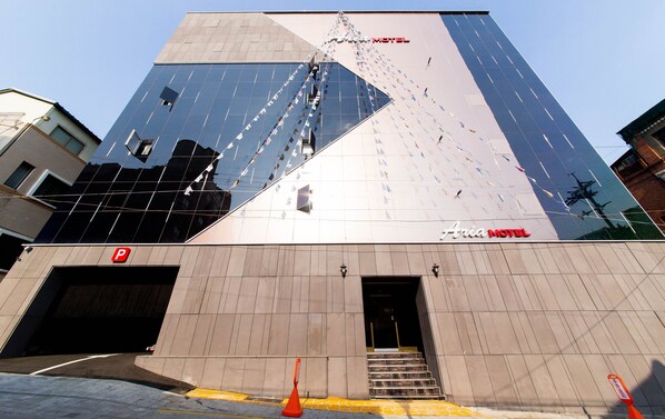 A modern hotel with a prominent glass facade and a visible entrance with steps leading up to the door. - Aria Motel (Busan)