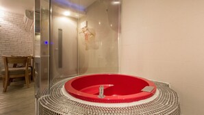 A modern bathroom with a glass-enclosed shower, a red bathtub, and a wooden chair. - Aria Motel (Busan)