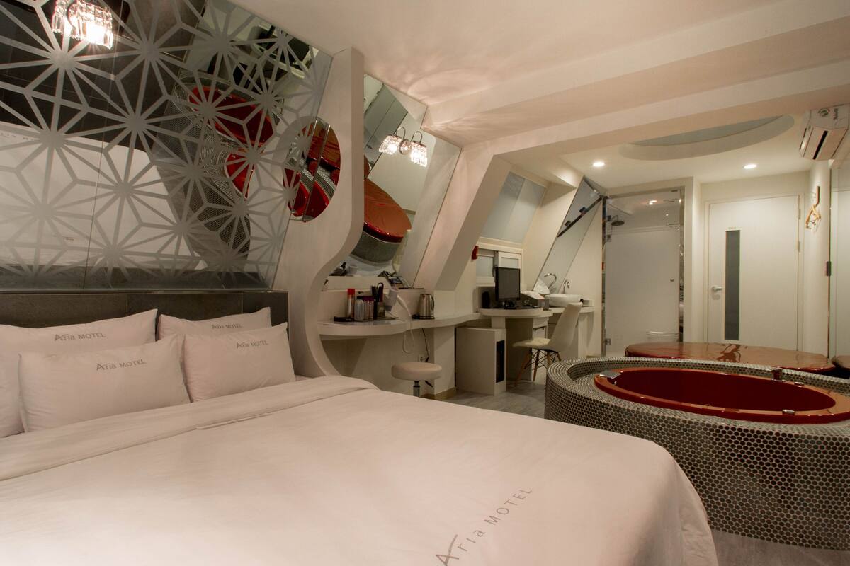A modern hotel room with a bed, a desk, a chair, a small bathroom, and a unique geometric wall design.