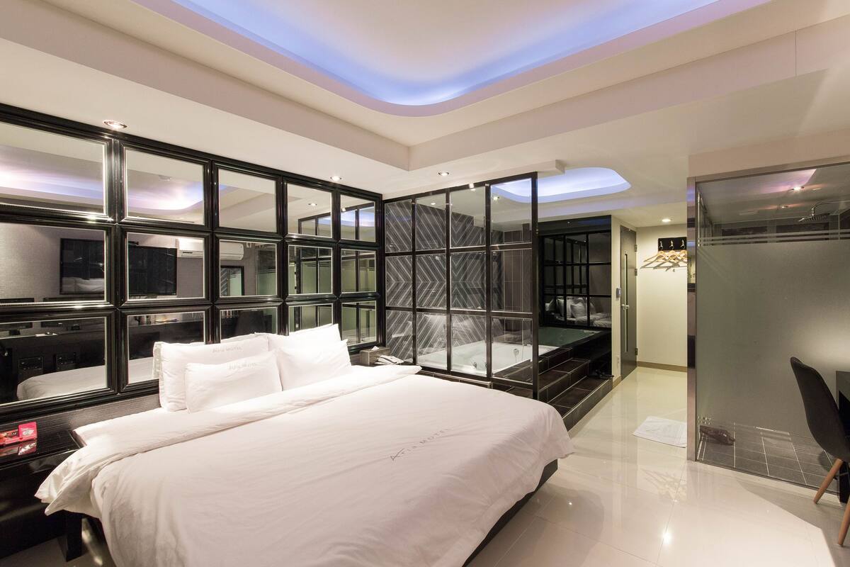 A modern hotel room with a large bed, a glass partition wall, and a separate shower area.