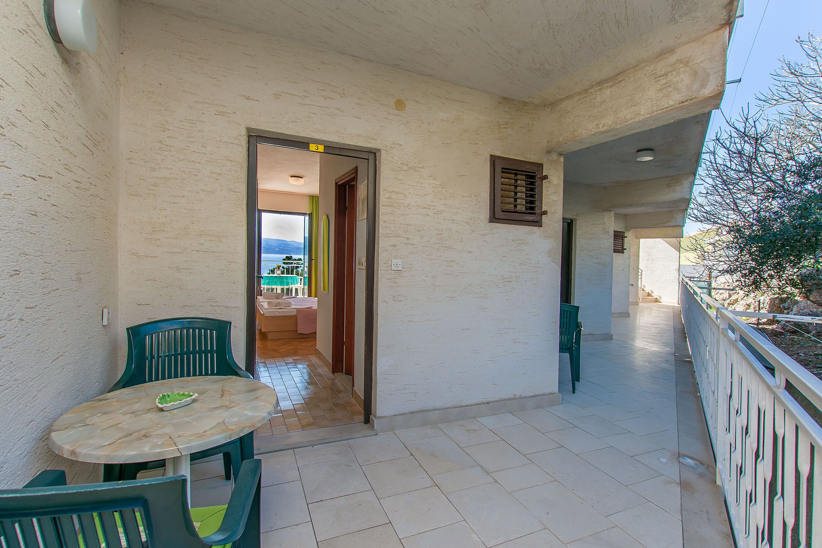 A balcony with a table and chairs, a door leading to an interior space, and a railing.