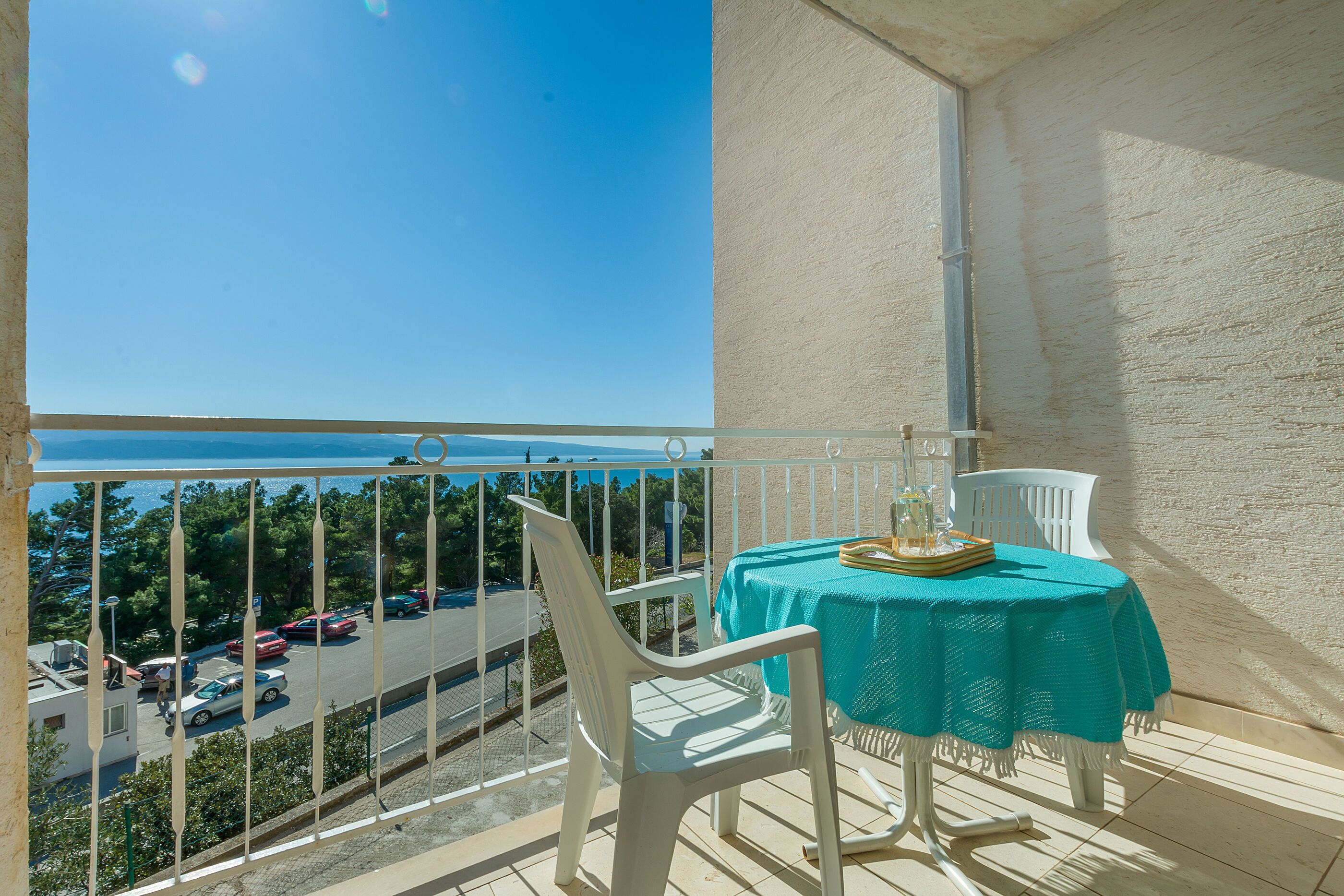 A balcony with a table and chairs, overlooking a parking area and trees.