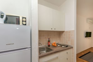 A compact kitchen with white cabinets, a Koncar refrigerator, a sink, and a countertop with a wine bottle and oranges. - Apartments Maras (Lokva Rogoznica)