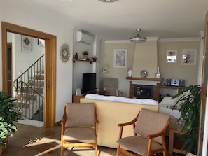 A living room with a sofa, two armchairs, a fireplace, a television, and a staircase.