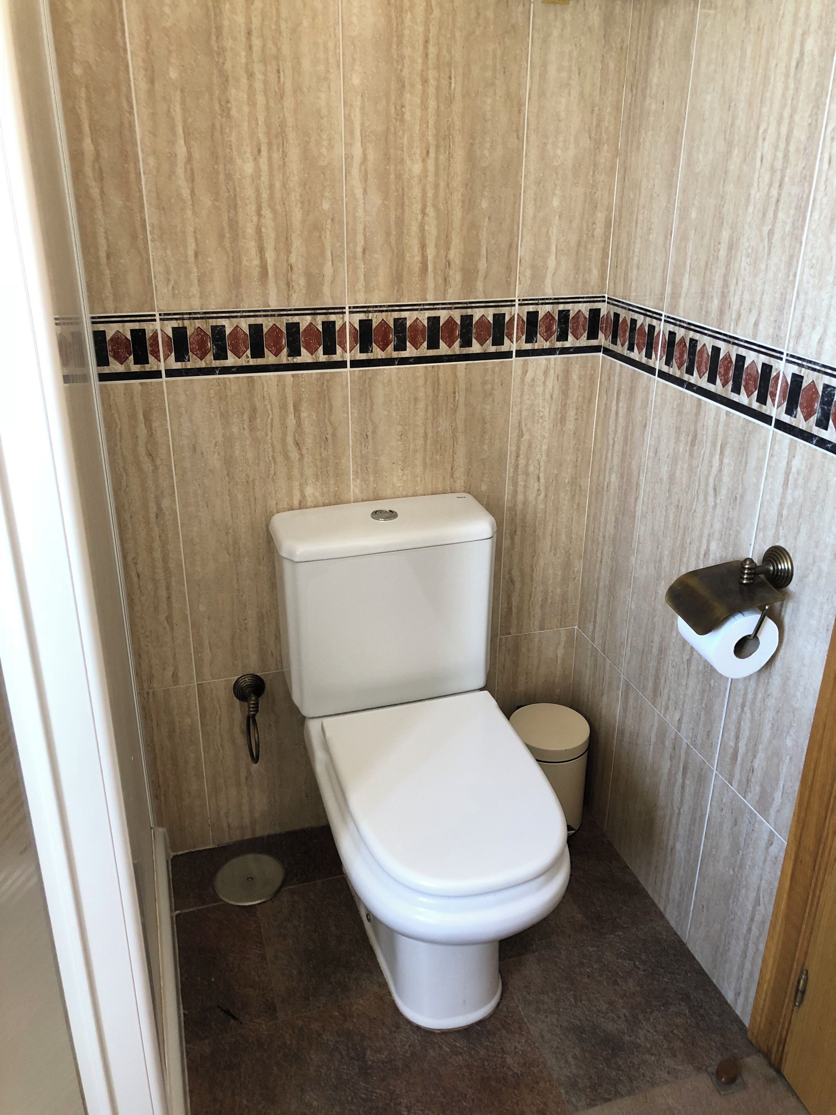 Une salle de bain équipée de toilettes, d’une petite poubelle et d’un porte-rouleau de papier toilette fixé au mur.