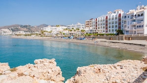 Un hotel frente al mar con varios pisos, balcones y una zona de playa con sombrillas y tumbonas.