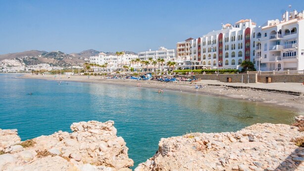 A coastal hotel with multiple floors, balconies, and a beach area with umbrellas and lounge chairs. - Villa Casa Rosi, ocean views, private pool, AC, and Wi-Fi (Nerja)