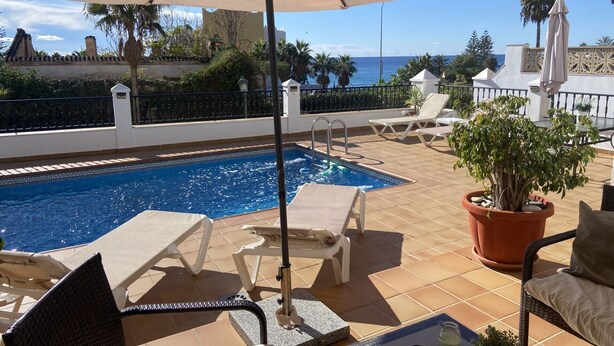 Un espace aménagé au bord de la piscine, comprenant une piscine, des chaises longues, un pot de fleurs et une vue sur l’océan.