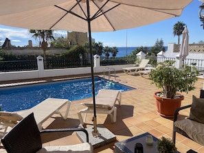 A poolside area with a swimming pool, lounge chairs, a potted plant, and a view of the ocean.