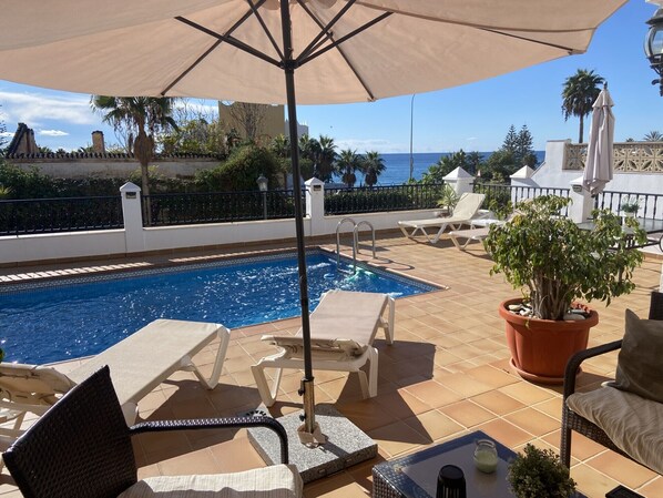 A poolside area with a swimming pool, lounge chairs, a potted plant, and a view of the ocean.