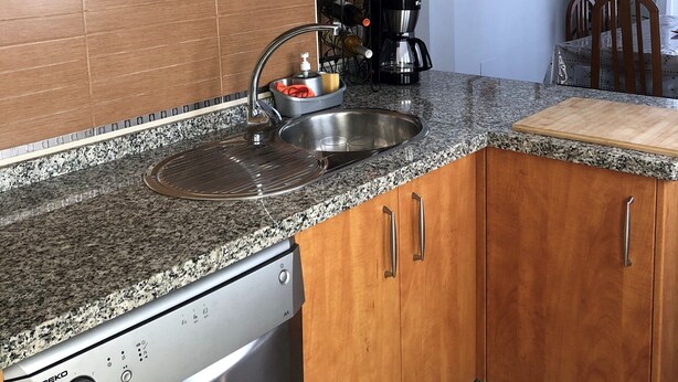 Una cocina con armarios de madera, lavavajillas de acero inoxidable, encimeras de granito y cafetera.