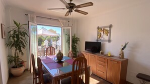 Un comedor con mesa, sillas, ventilador de techo, televisor y aparador.