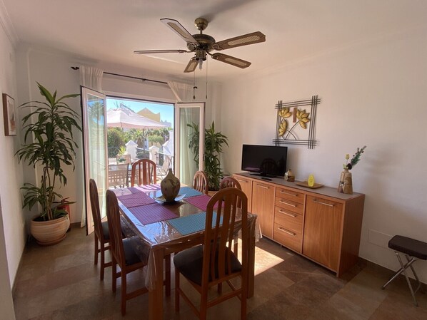 Un espace repas comprenant une table, des chaises, un ventilateur de plafond, un téléviseur et un meuble.