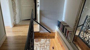 A wooden staircase with a black railing, a white door at the top, and a bookshelf with books on the right side. - Maison de Campagne et Nature (Quincy-sous-le-Mont)