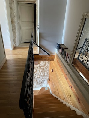Een houten trap met een zwarte leuning, een witte deur aan de bovenkant en een boekenkast met boeken aan de rechterkant.