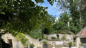 A stone-walled courtyard with a grassy lawn, outdoor furniture, and potted plants. - Maison de Campagne et Nature (Quincy-sous-le-Mont)