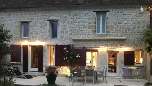 A stone building with multiple windows, a door, and a small outdoor seating area with chairs and a table. - Maison de Campagne et Nature (Quincy-sous-le-Mont)
