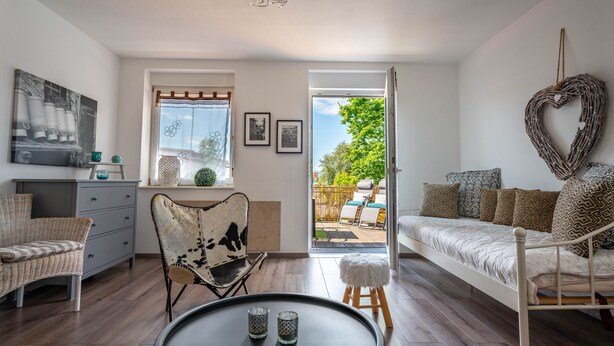 A cozy living room with a sofa, a chair, a small table, and a view of the outdoors.