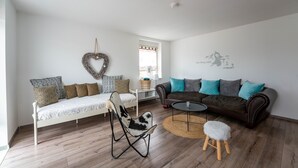 A modern living room with a white sofa, a brown leather couch, a white rocking chair, a small round table, and a stool.