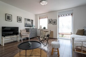 A modern living room with a flat-screen TV, a round coffee table, a sofa, a chair, a small stool, and a bed.