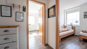 A bedroom with a wooden bed, a small desk, and a dresser. There are framed certificates on the wall and a window with a view of the outside.