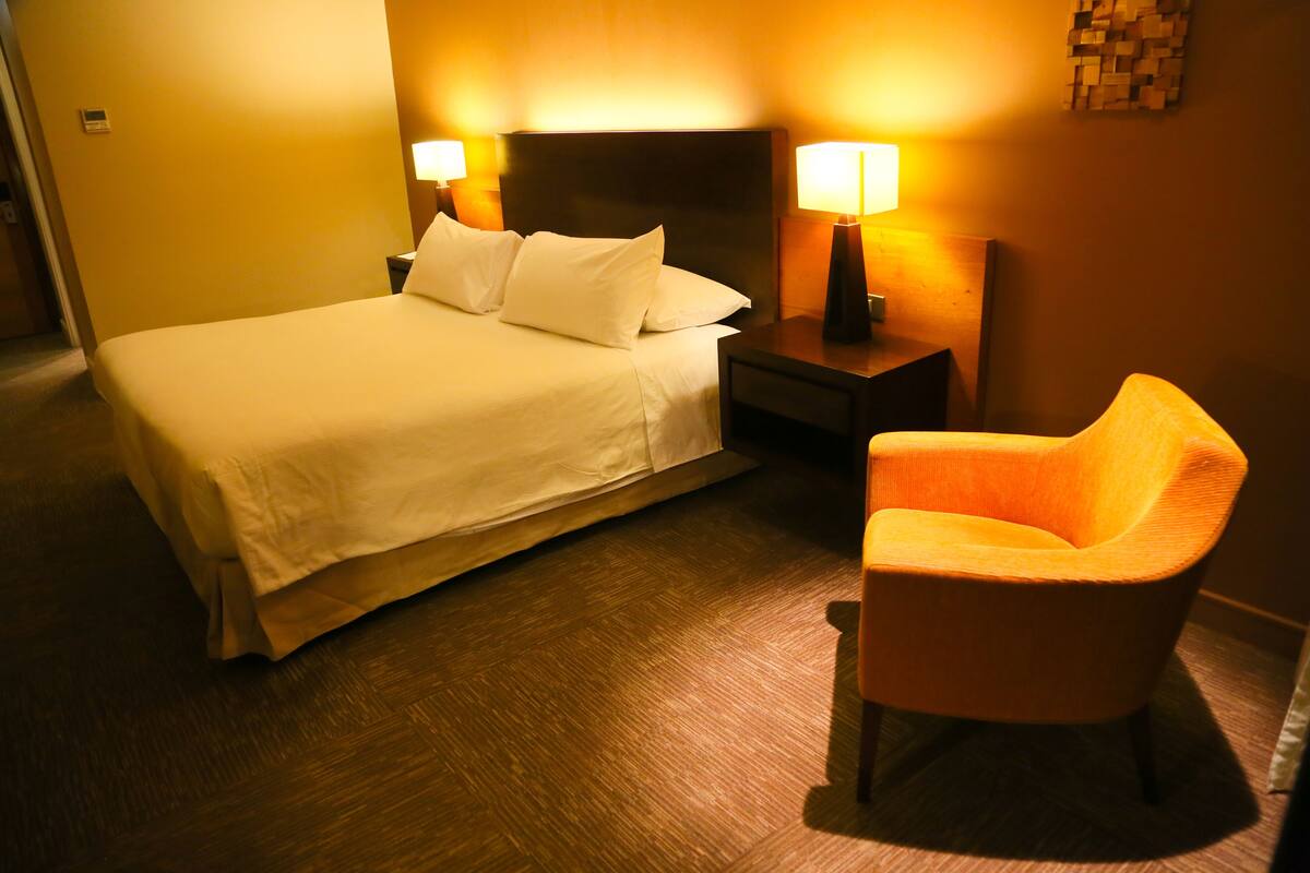 A hotel room with a bed, two bedside lamps, a nightstand, and a single orange chair.