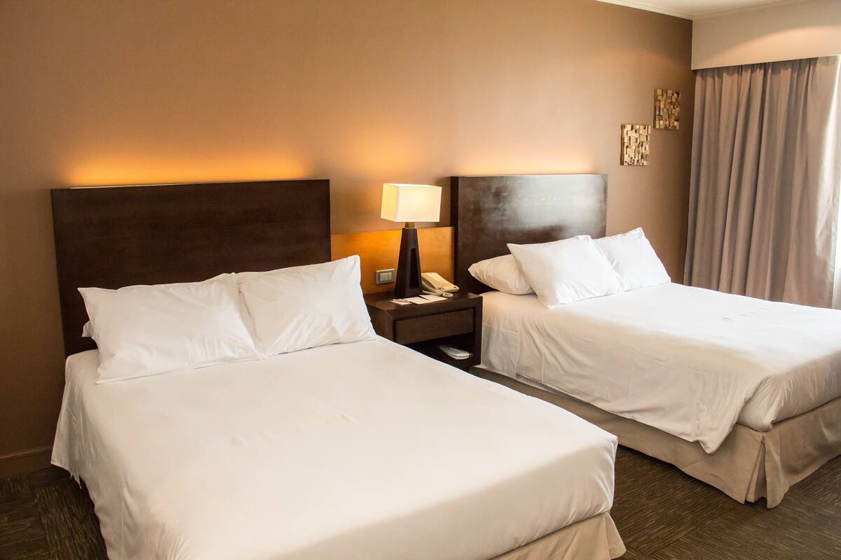 A hotel room with two beds, a nightstand with a lamp, and a telephone.