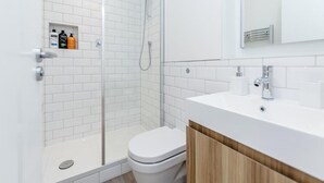 Une salle de bain moderne avec une douche à parois de verre, des toilettes blanches et un meuble-lavabo en bois avec un lavabo blanc.