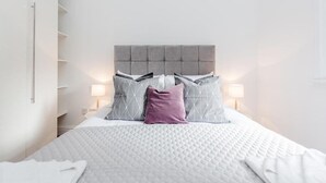 Une chambre à coucher bien rangée, avec un lit, des oreillers et des lampes de chevet.