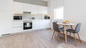 Une cuisine moderne avec des meubles blancs, un four encastré et un coin repas comprenant une table et des chaises.