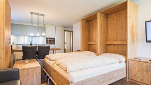 A compact room with a wooden bed, a small desk, and a kitchenette.