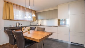 A modern kitchen with a wooden dining table, black chairs, and stainless steel appliances.