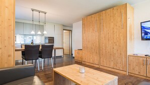 A modern kitchen with wooden cabinets, a dining area with a table and chairs, and a TV mounted on the wall.