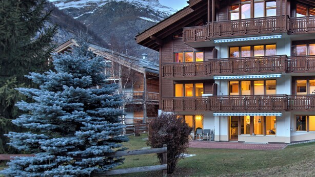 A multi-story wooden building with balconies, a snow-covered mountain in the background, and a logo for "Clean & Safe" in the bottom right corner. - Apartment for 2 to 4 people in Zermatt (Zermatt)