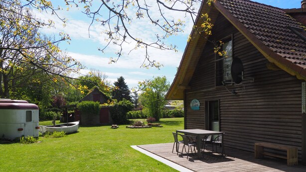 A wooden cabin with a patio, a small boat, and a well-maintained lawn. - Wassersportlers Traum (Wiek)