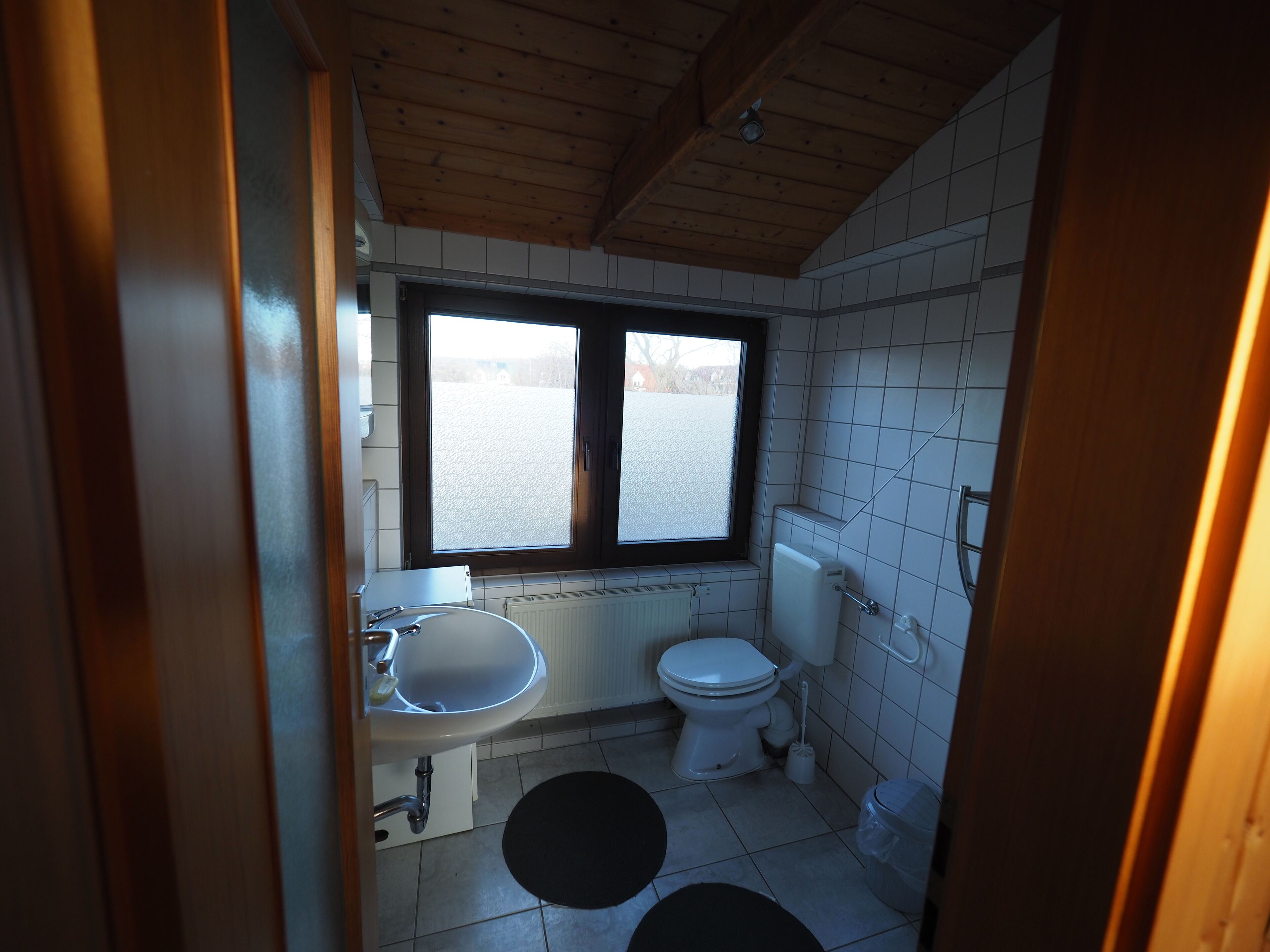 Une petite salle de bain compacte, dotée d’une fenêtre, d’un lavabo, de toilettes et d’un radiateur.