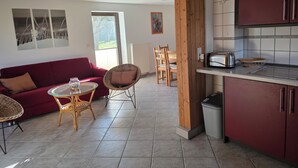 A modern kitchen with wooden cabinets, a dining area with wicker chairs, a red sofa, and a glass table. - Wassersportlers Traum (Wiek)
