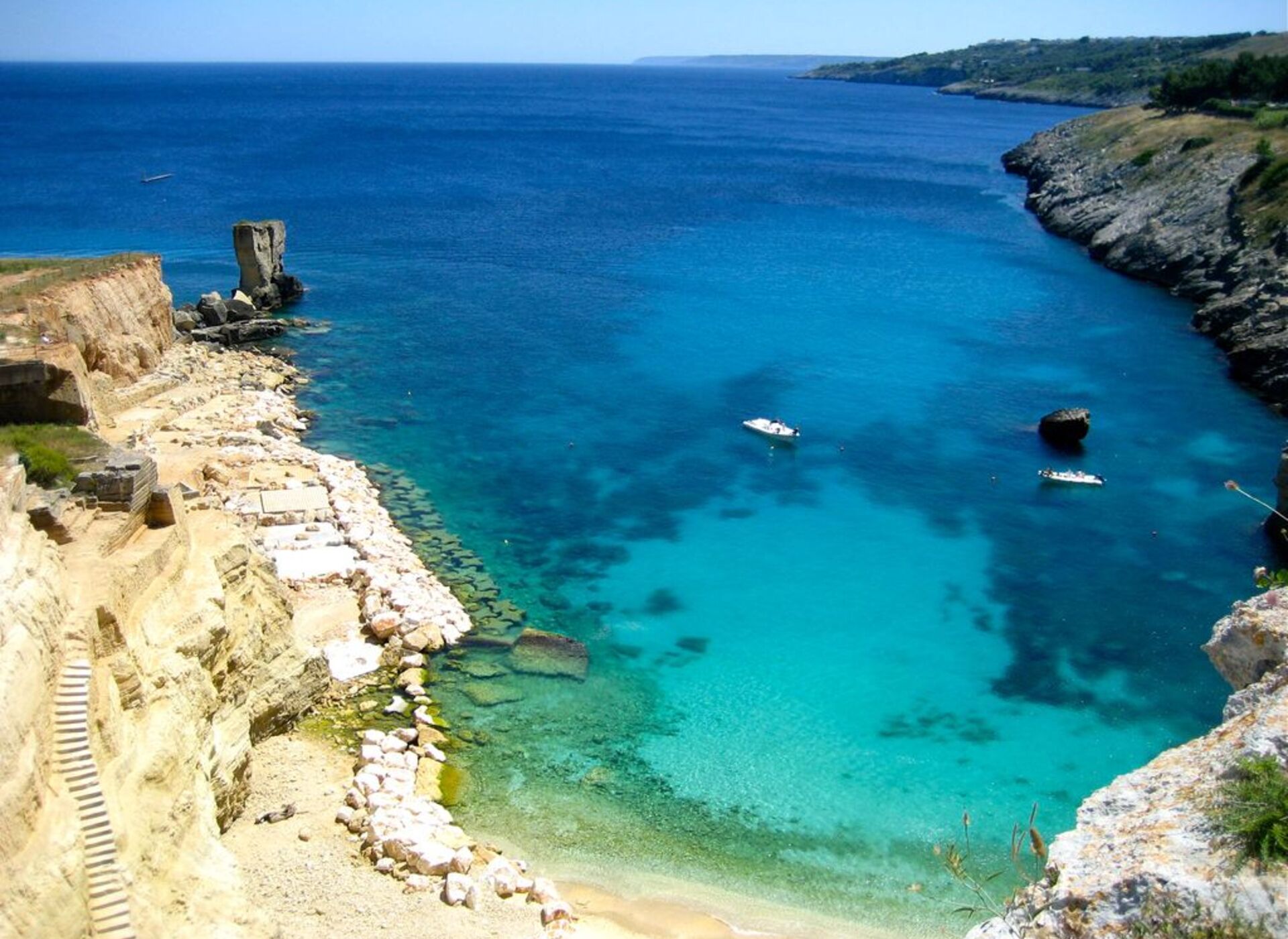 Un paisaje costero con aguas azul cristalino, acantilados rocosos y un pequeño bote.
