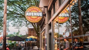 An outdoor seating area with tables and chairs, a neon sign reading "AVENUE," and a brick building facade. - Stylish Bungalow | Near Cooper-Young, Eats & Beats (Memphis)