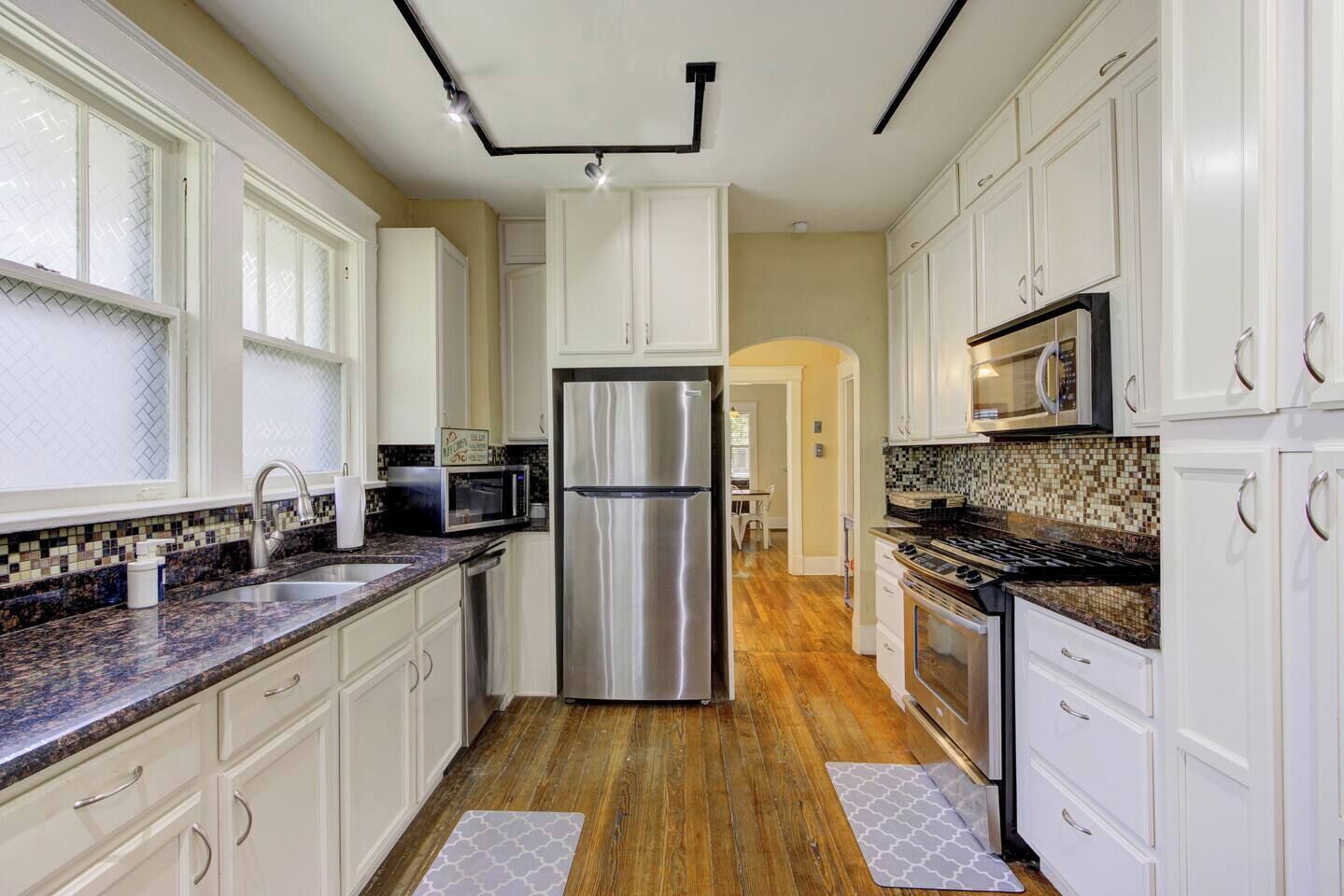 A modern kitchen with white cabinets, stainless steel appliances, and a wooden floor.