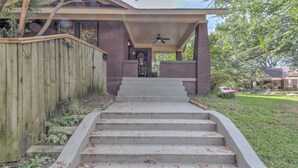 A house with a covered front porch, a brick exterior, and a concrete staircase leading to the entrance. - Stylish Bungalow | Near Cooper-Young, Eats & Beats (Memphis)