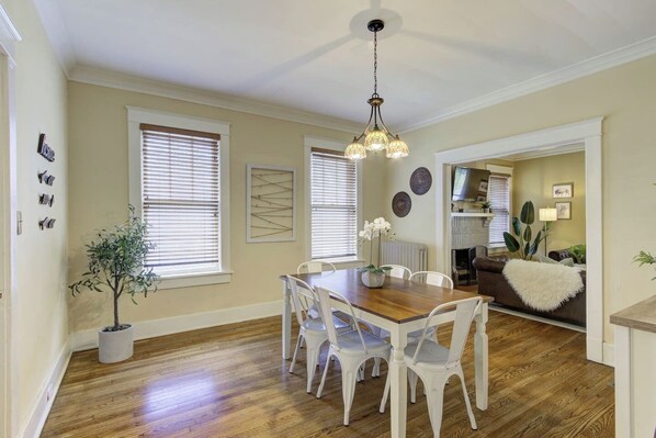 Un coin repas avec une table en bois et des chaises blanches, une plante en pot et un luminaire suspendu au plafond.