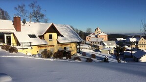 A snow-covered village with traditional buildings, including a prominent yellow house with a red roof and a church with a tower.