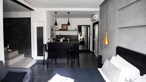 A modern hotel room with a large bed, a dining area, and a kitchen in the background.