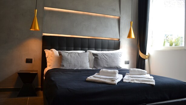 A modern hotel room with a dark blue bed, white pillows, and a neatly folded towel on the bed.