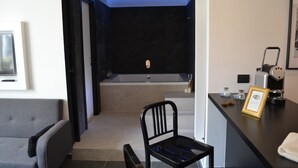 A modern bathroom with a bathtub, a chair, and a counter with a framed certificate.