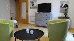 Ett rum med en säng, en tv på en byrå, två stolar och ett litet bord med två koppar.