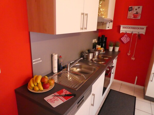 A modern kitchen with white cabinets, stainless steel appliances, and a red accent wall. - Allgäutraum Ferienwohnung Nr. 3 für 2-6 Personen (Durach-Weidach)