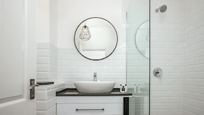 A modern bathroom with a white sink, a round mirror, and a glass shower enclosure.